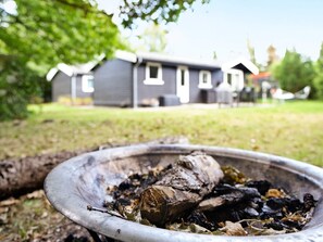 A metal bowl with a log and ashes, set outdoors with a house in the background. - 6 Person Holiday Home in Hojby (Hojby)