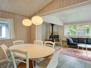 A cozy interior with a round dining table, white chairs, a black leather sofa, and a wood-paneled room with a fireplace. - 6 Person Holiday Home in Hojby (Hojby)