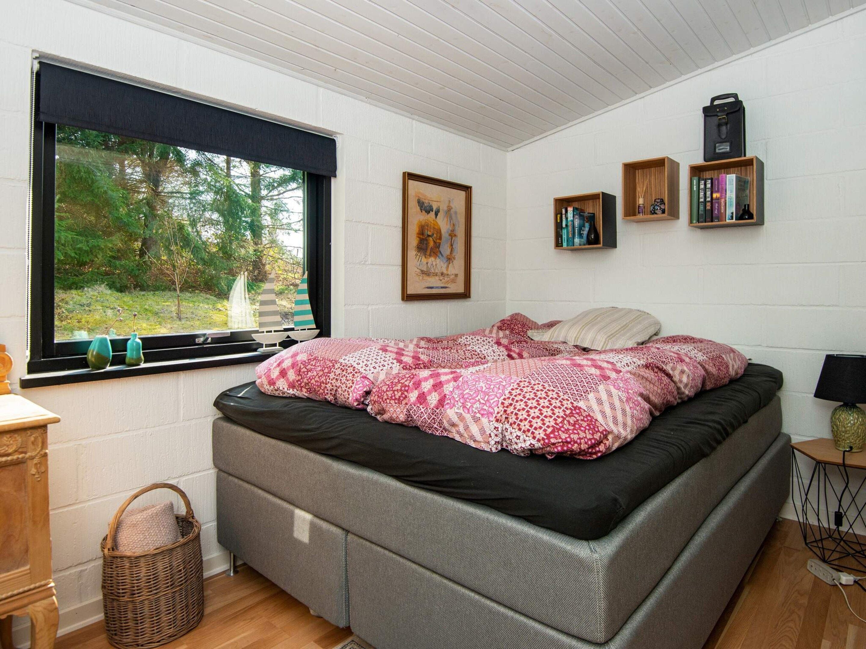 Une chambre à coucher avec un lit, une fenêtre donnant sur des arbres, une bibliothèque et une lampe.