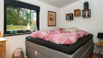 Une chambre à coucher avec un lit, une fenêtre donnant sur des arbres, une bibliothèque et une lampe.