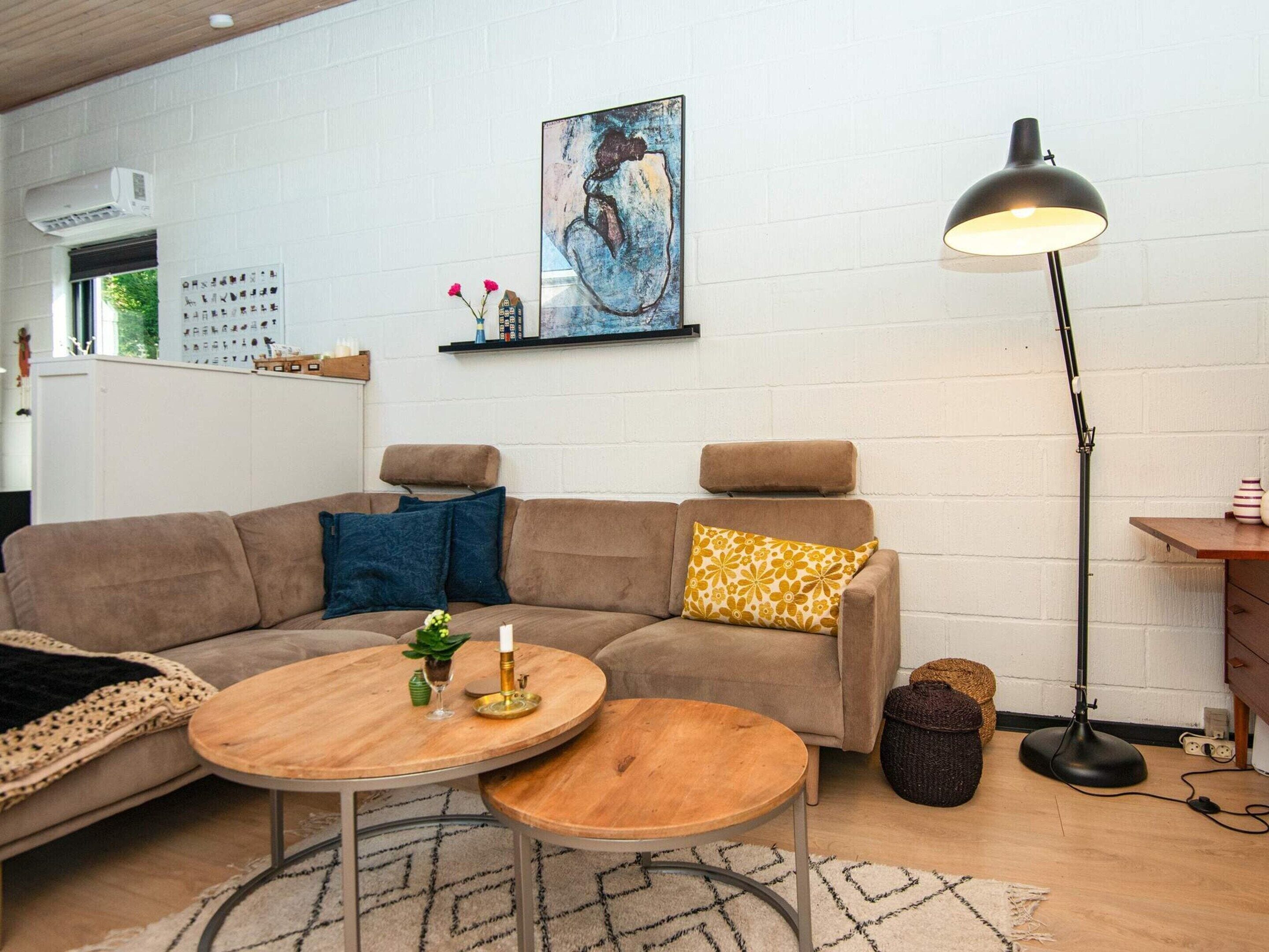 Una sala de estar moderna con un sofá modular, dos mesas redondas de madera, una lámpara de pie y un cuadro en la pared.