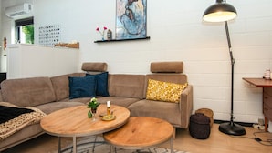 A modern living room with a sectional sofa, two round wooden tables, a floor lamp, and a painting on the wall. - 4 Star Holiday Home in Ebeltoft (Ebeltoft)