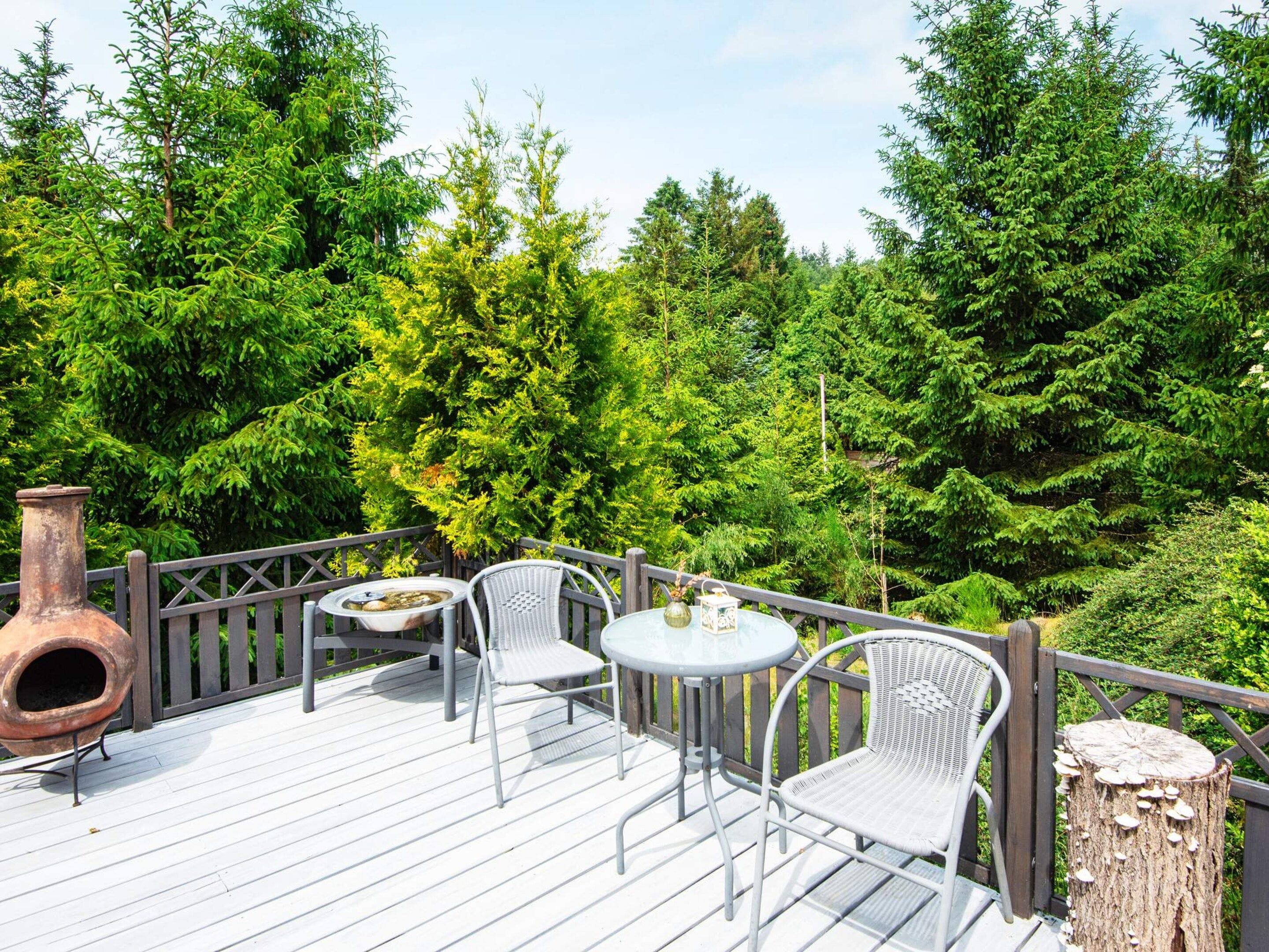 A wooden deck with outdoor furniture, surrounded by dense greenery.