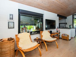 A modern living room with wicker chairs, a flat-screen TV, and a kitchen area.