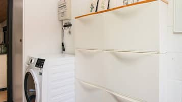 Un cuarto de lavandería con una lavadora de carga frontal, un armario de servicios y una estantería con objetos decorativos.
