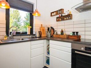 A kitchen with a window, a sink, a stove, and wooden shelves with kitchen items. - 4 Star Holiday Home in Ebeltoft (Ebeltoft)