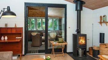 A cozy living room with a fireplace, wooden furniture, and a view through a glass door.