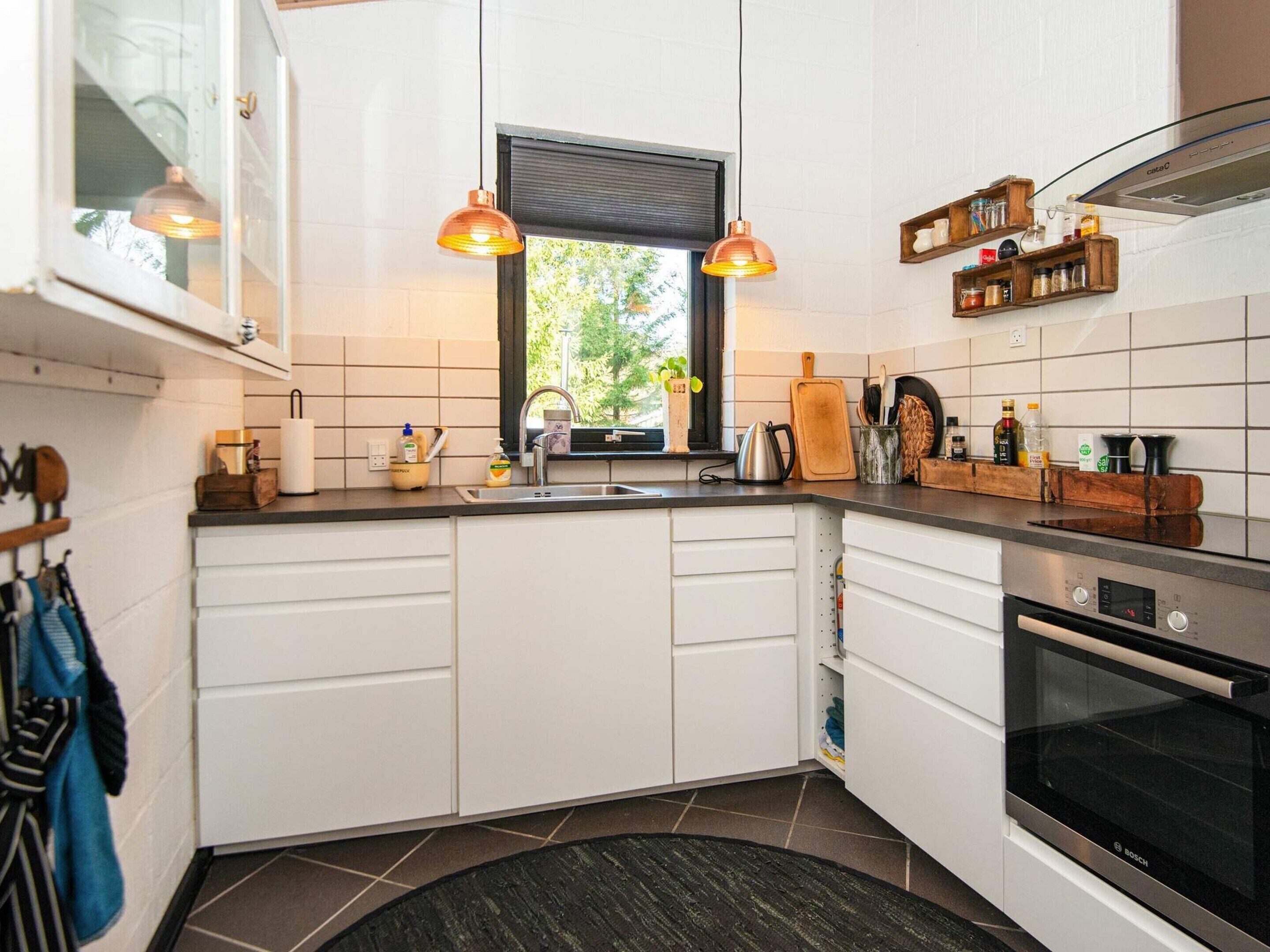 A modern kitchen with white cabinets, a Bosch oven, a window with a view, and pendant lights.