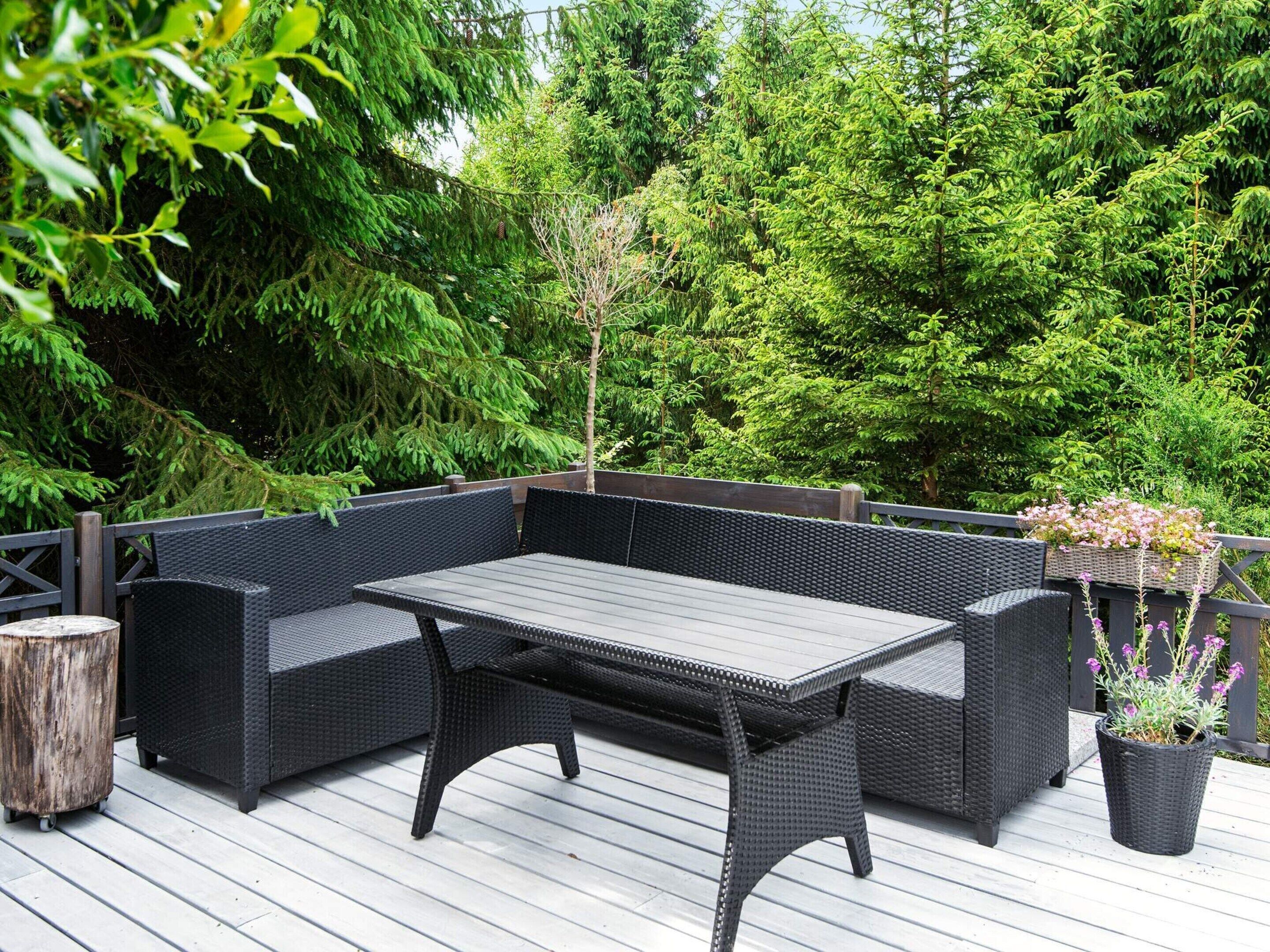 Eine Terrasse mit einer dunklen Rattan-Sitzgruppe, einem Holztisch und einem Blumentopf mit Blumen.