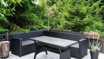 A deck with a dark wicker sofa set, a wooden table, and a potted plant with flowers.