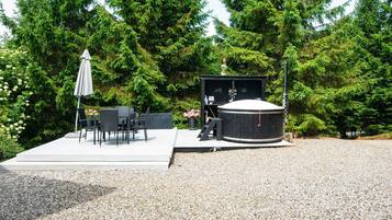 Un bain à remous doté d’une terrasse en bois, entouré d’arbres et agrémenté d’un espace patio avec des meubles d’extérieur.