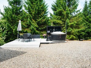 A hot tub with a wooden deck, surrounded by trees and a patio area with outdoor furniture. - 4 Star Holiday Home in Ebeltoft (Ebeltoft)