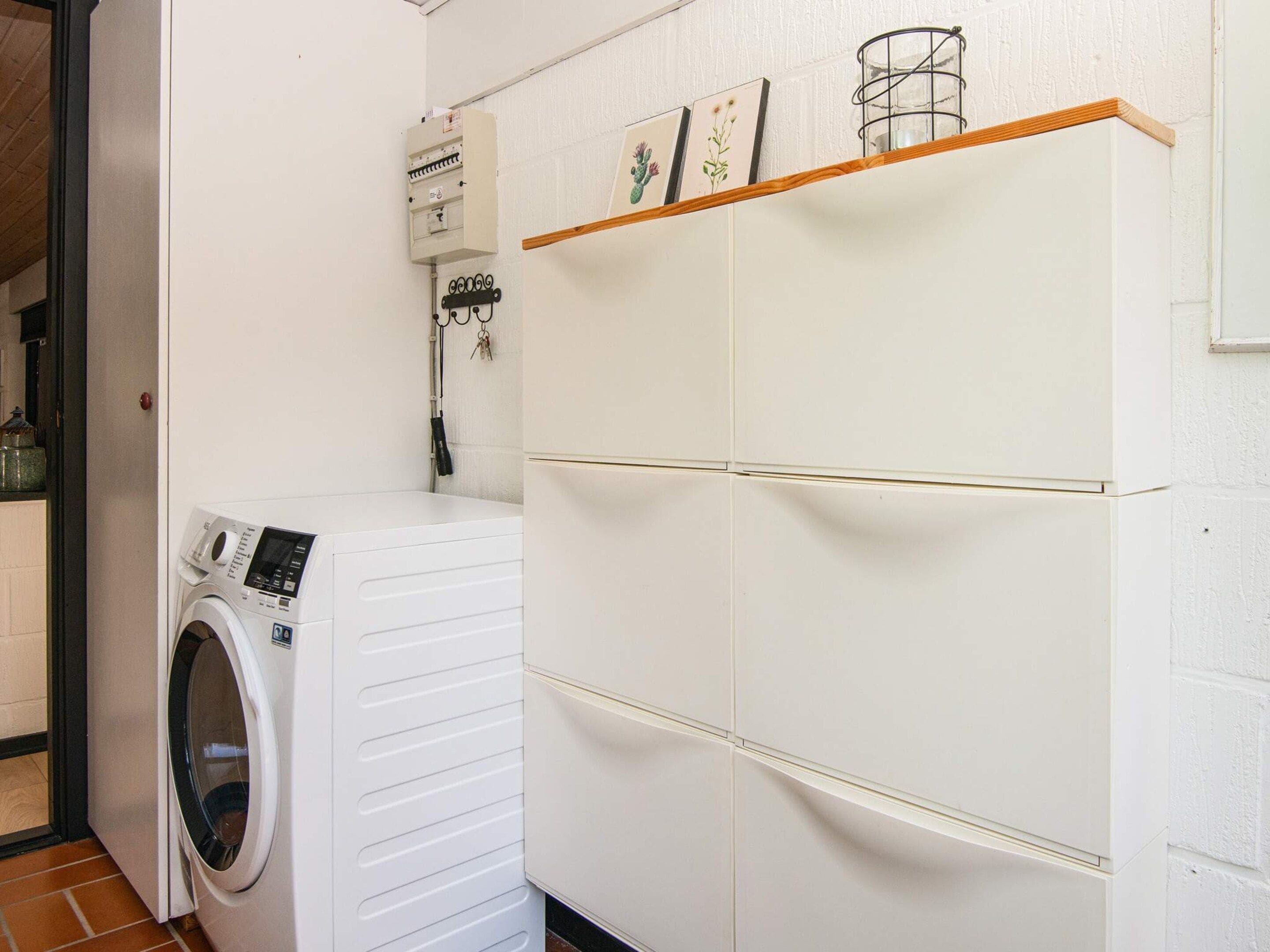 Une buanderie équipée d’un lave-linge à chargement frontal, d’un compteur et d’une étagère où sont exposés des tableaux encadrés.