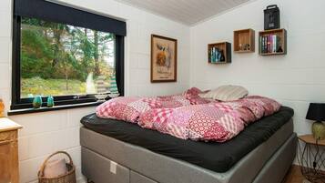 A bedroom with a bed, a window with a view of trees, a bookshelf, and a lamp.