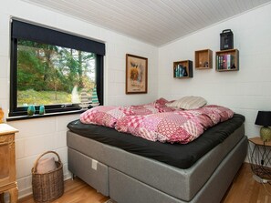 A bedroom with a bed, a window with a view of trees, a bookshelf, and a lamp. - 4 Star Holiday Home in Ebeltoft (Ebeltoft)