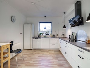 A modern kitchen with white cabinets, a built-in dishwasher, a window with plants, and a dining area with a chair and table. - 8 Person Holiday Home in Nysted (Nysted)