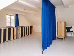 A room with a sloped ceiling, a wooden bench, a black chair, and a blue curtain. - 8 Person Holiday Home in Nysted (Nysted)