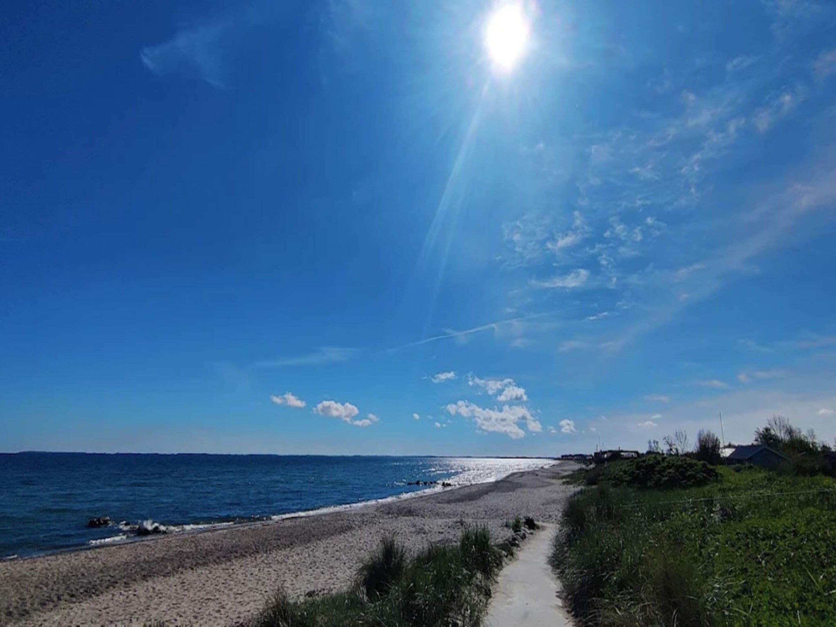 A beach with a clear sky, a path leading to the water, and distant buildings.
