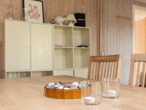 A wooden table with a bowl of snacks, two clear glasses with candles, and a white cabinet in the background. - 8 Person Holiday Home in Otterup (Otterup)