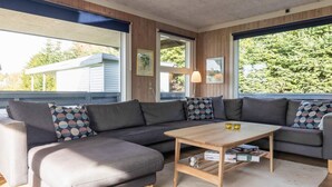 A modern living room with a sectional sofa, a wooden coffee table, and large windows with a view of greenery. - 8 Person Holiday Home in Otterup (Otterup)