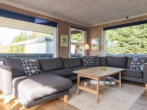 A modern living room with a sectional sofa, a wooden coffee table, and large windows with a view of greenery. - 8 Person Holiday Home in Otterup (Otterup)