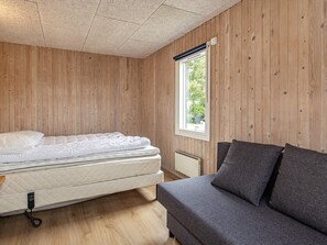 A room with a bed, a grey sofa, wooden walls, and a window with a view of greenery. - 8 Person Holiday Home in Otterup (Otterup)