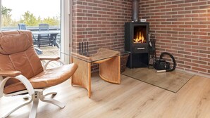 A room with a brick wall, a glass table, a leather chair, and a wood-burning stove. - 8 Person Holiday Home in Otterup (Otterup)