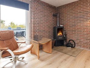 A room with a brick wall, a glass table, a leather chair, and a wood-burning stove. - 8 Person Holiday Home in Otterup (Otterup)