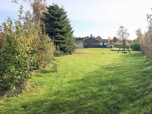 A residential property with a grassy yard, a swing set, and a house with a dark roof and white walls.
