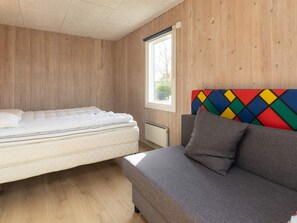 A room with a bed, a sofa, wooden walls, a window, and a radiator. - 8 Person Holiday Home in Otterup (Otterup)