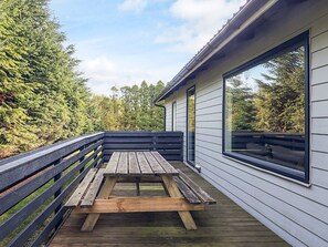 En træterrasse med et picnicbord, omgivet af et gelænder, med udsigt over et skovområde.