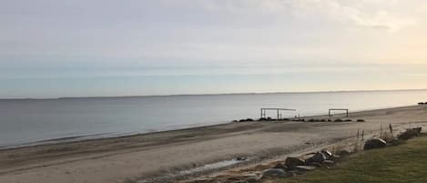 Una playa con una zona cubierta de césped, un sendero de arena y una construcción cerca del agua.