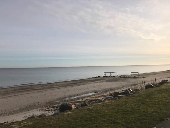 A beach with a grassy area, a sandy path, and a structure near the water.
