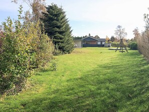 A residential property with a well-maintained lawn, a swing set, and a house with a dark roof and white walls.