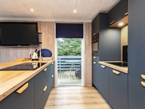 Una cocina moderna con encimera de madera, armarios oscuros y un televisor montado sobre la encimera.