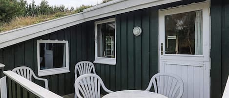 A small, dark green wooden building with white trim, a round table, and four white chairs.