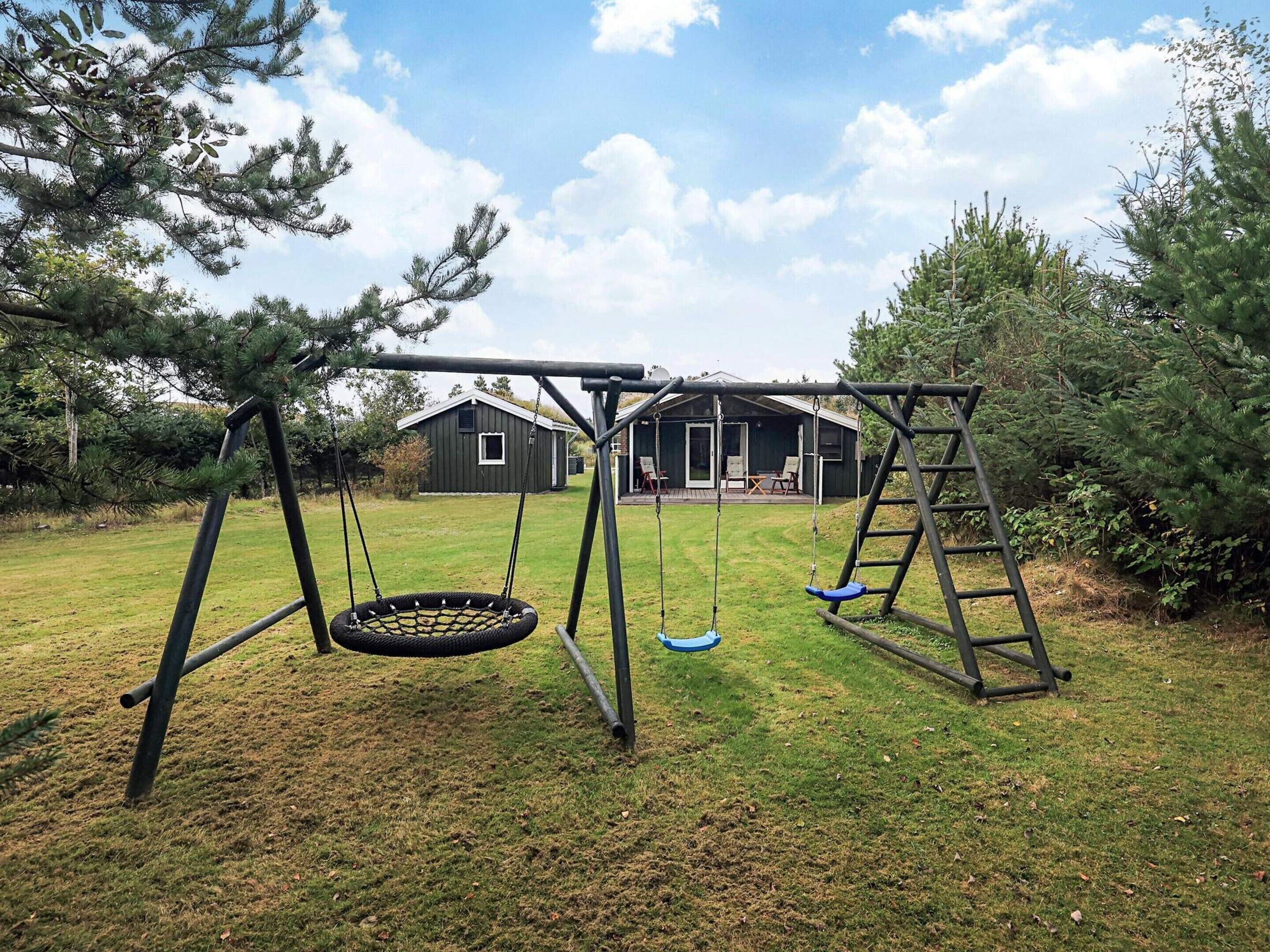 A swing set with a tire swing and a ladder, a grassy yard, and a wooden building with a porch.