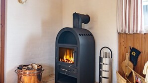 A room with a wood-burning stove, a metal pot, and a wicker basket with magazines. - 6 Person Holiday Home in Blokhus (Blokhus)