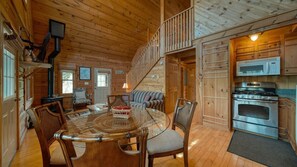 A cozy cabin interior with a dining table, chairs, a sofa, a staircase, and a kitchen area with a microwave and stove. - Creekside Fish Cabin (Hiawassee)