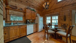 A wooden cabin interior with a kitchen, dining area, and a large window. - Creekside Fish Cabin (Hiawassee)