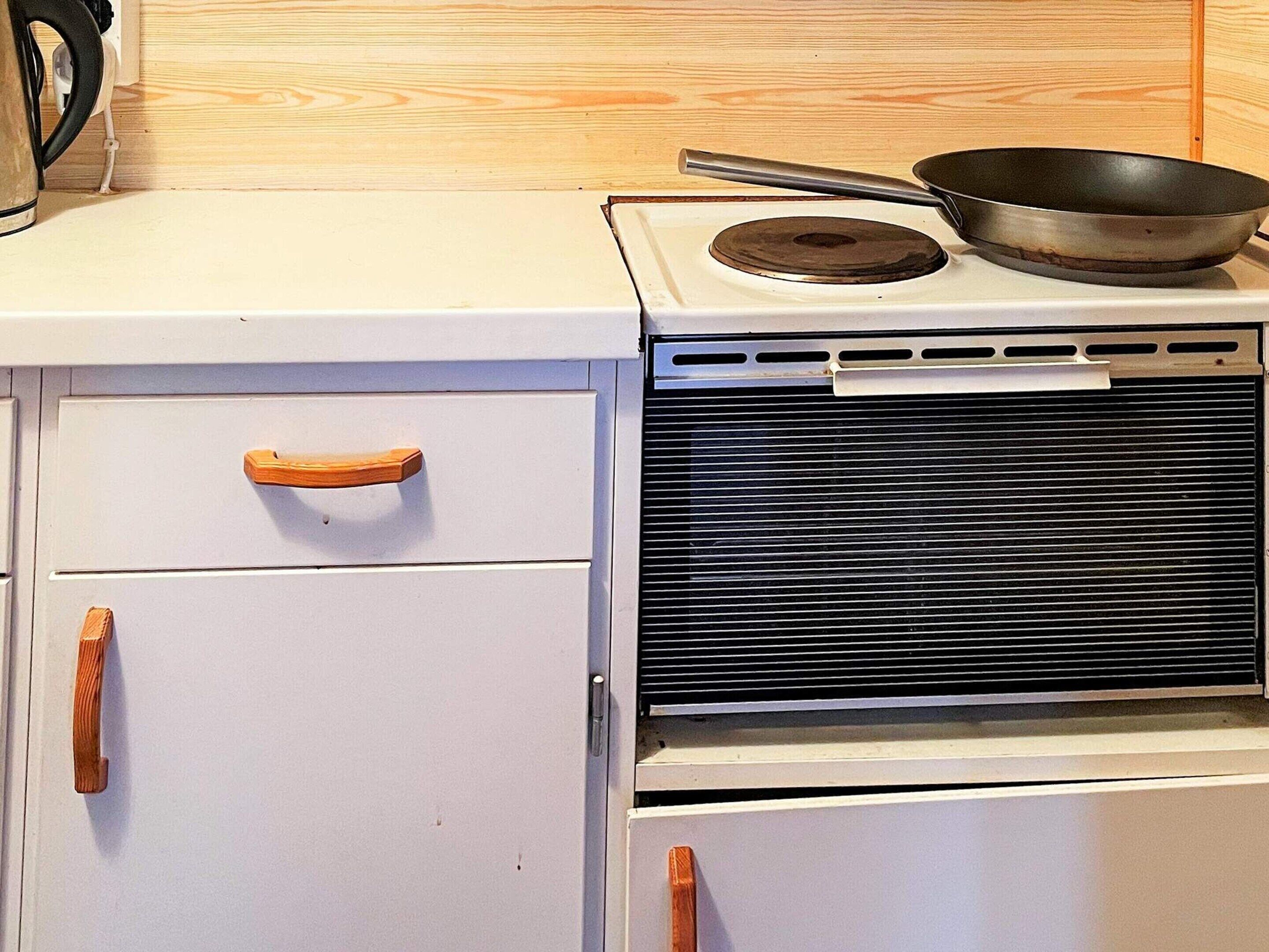 A white kitchen stove with a frying pan on top and wooden handles on the cabinets.