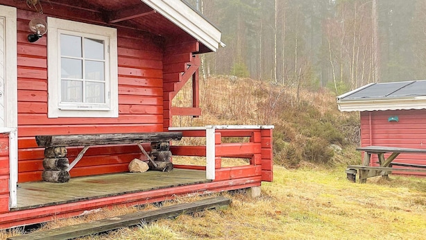A red wooden cabin with a white-framed window, a porch with a wooden bench, and a small table. - 5 Person Holiday Home in Sexdrega-by Traum (Sexdrega)