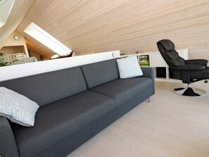 A modern living room with a grey sofa, a black leather chair, and a wooden ceiling.