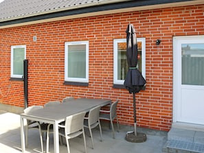 A patio with a table and chairs, a covered umbrella, and a brick wall with windows. - 10 Person Holiday Home in Hadsund (Hadsund)