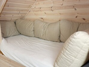 Habitació amb sostre de fusta inclinat i un llit amb roba de llit beix.