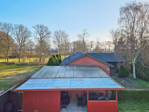 A red barn with a metal roof, a smaller attached structure, and a grassy field with trees in the background. - 10 Person Holiday Home in Hadsund (Hadsund)