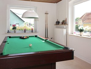 A pool table with a green felt surface, a white overhead lamp, and a window with a view of a building and greenery outside. - 10 Person Holiday Home in Hadsund (Hadsund)