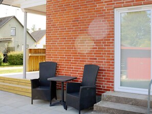 An outdoor patio with two chairs and a table, a brick wall, and a window with blinds.