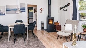 A modern living room with a wooden floor, a dining area with a table and chairs, a fireplace, and a window with curtains. - 6 Person Holiday Home in Orsted (Ørsted)