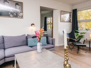 A modern living room with a grey sofa, a coffee table, and a vase with flowers. There is a framed picture on the wall and a lamp on a side table. - 6 Person Holiday Home in Orsted (Ørsted)